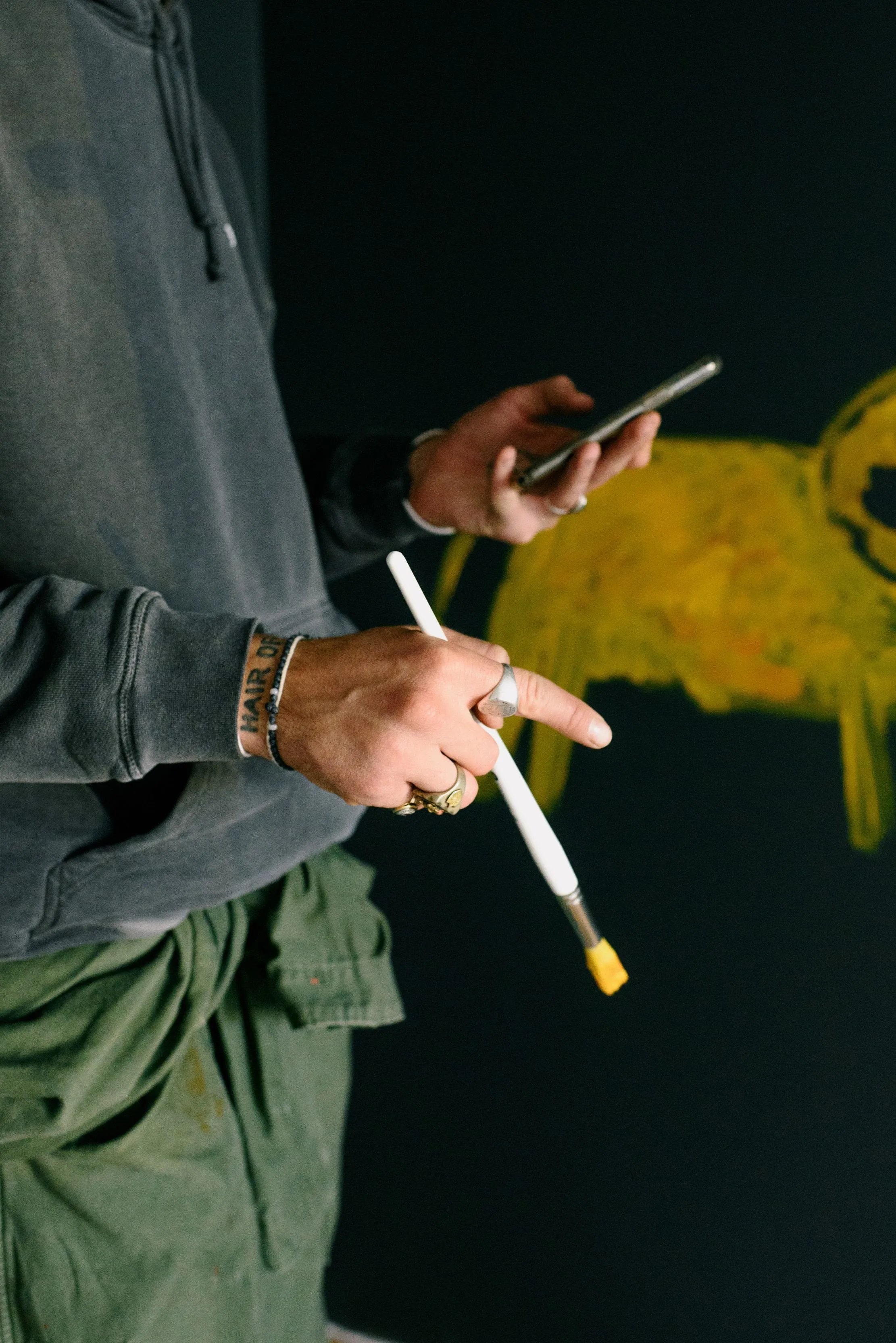 An artist holding a paintbrush and phone in front of a work in progress