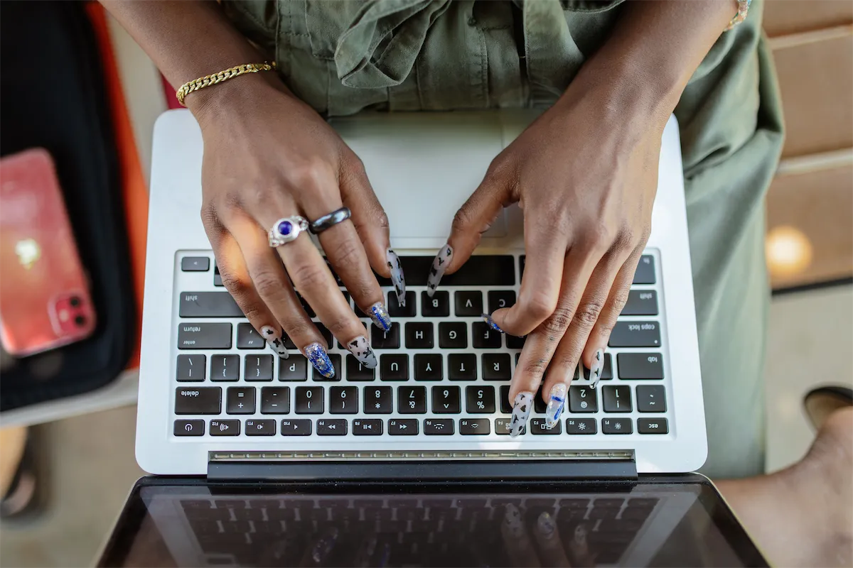 Hands with painted nails typing on a laptop, seen from above