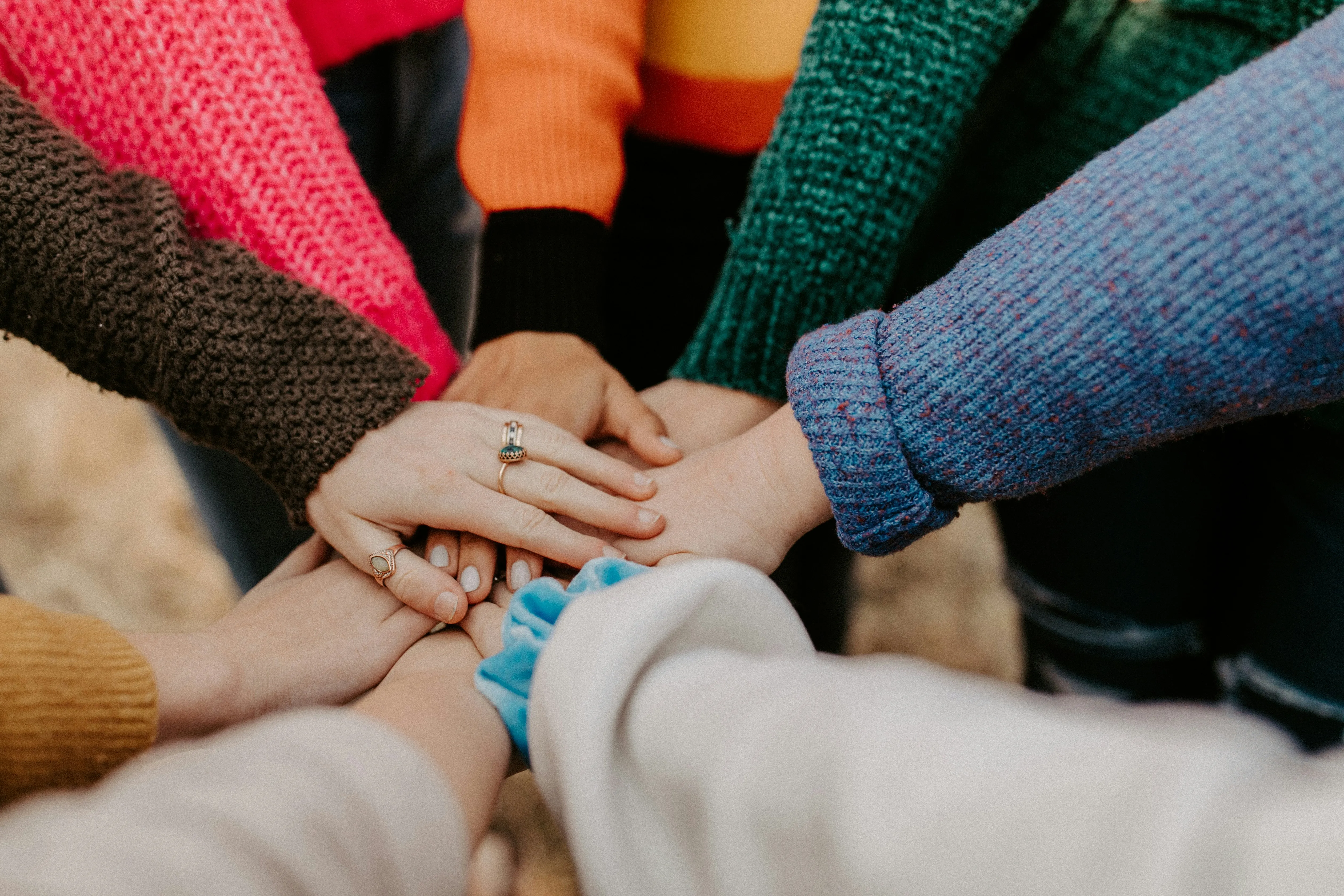 A diverse group of people in colorful sweaters stacking their hands together