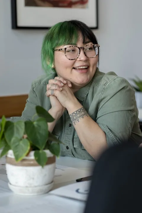 An Indigenous woman with a banded forearm tattoo smiling at a meeting table