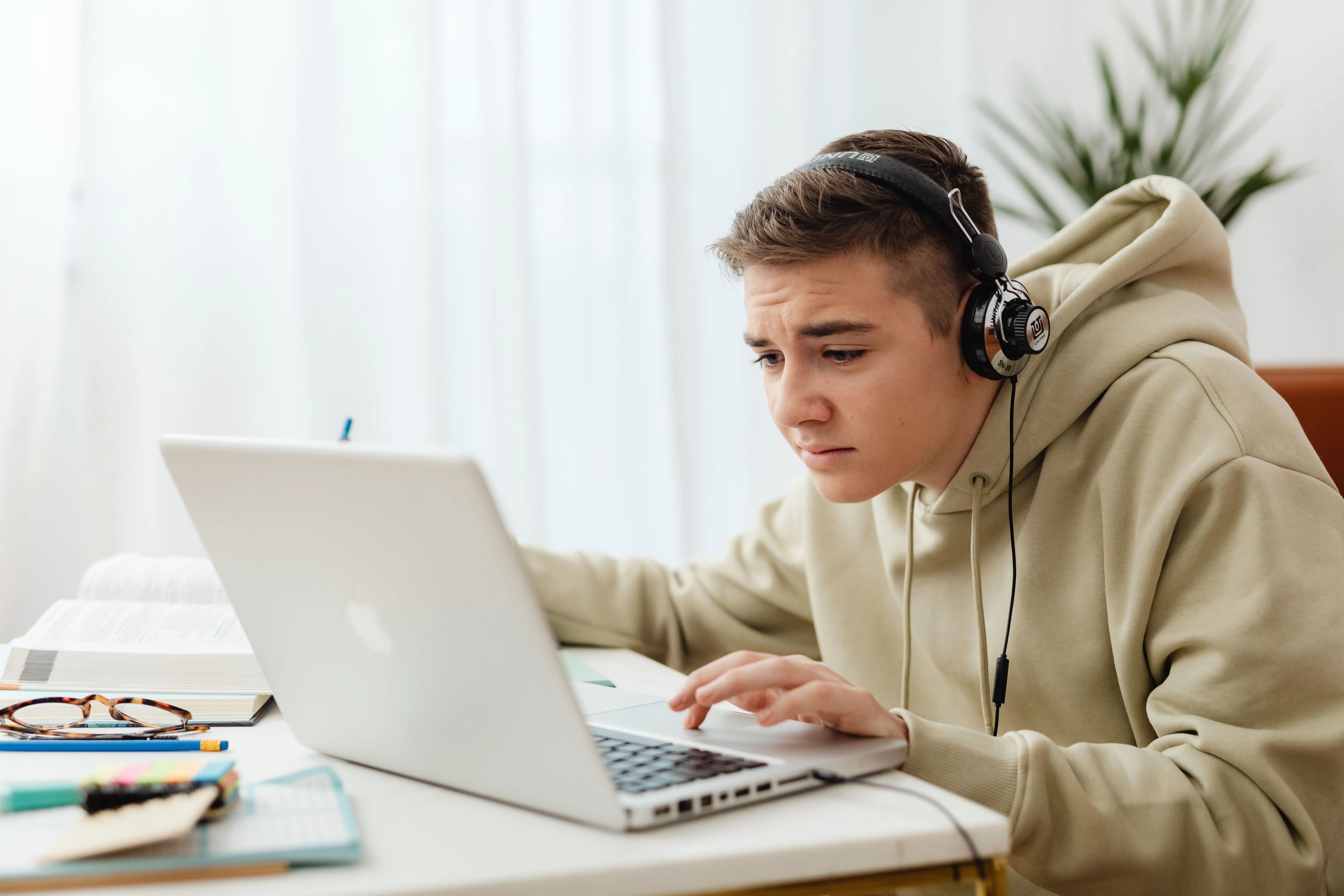 A young person wearing headphones working intently at a laptop at home