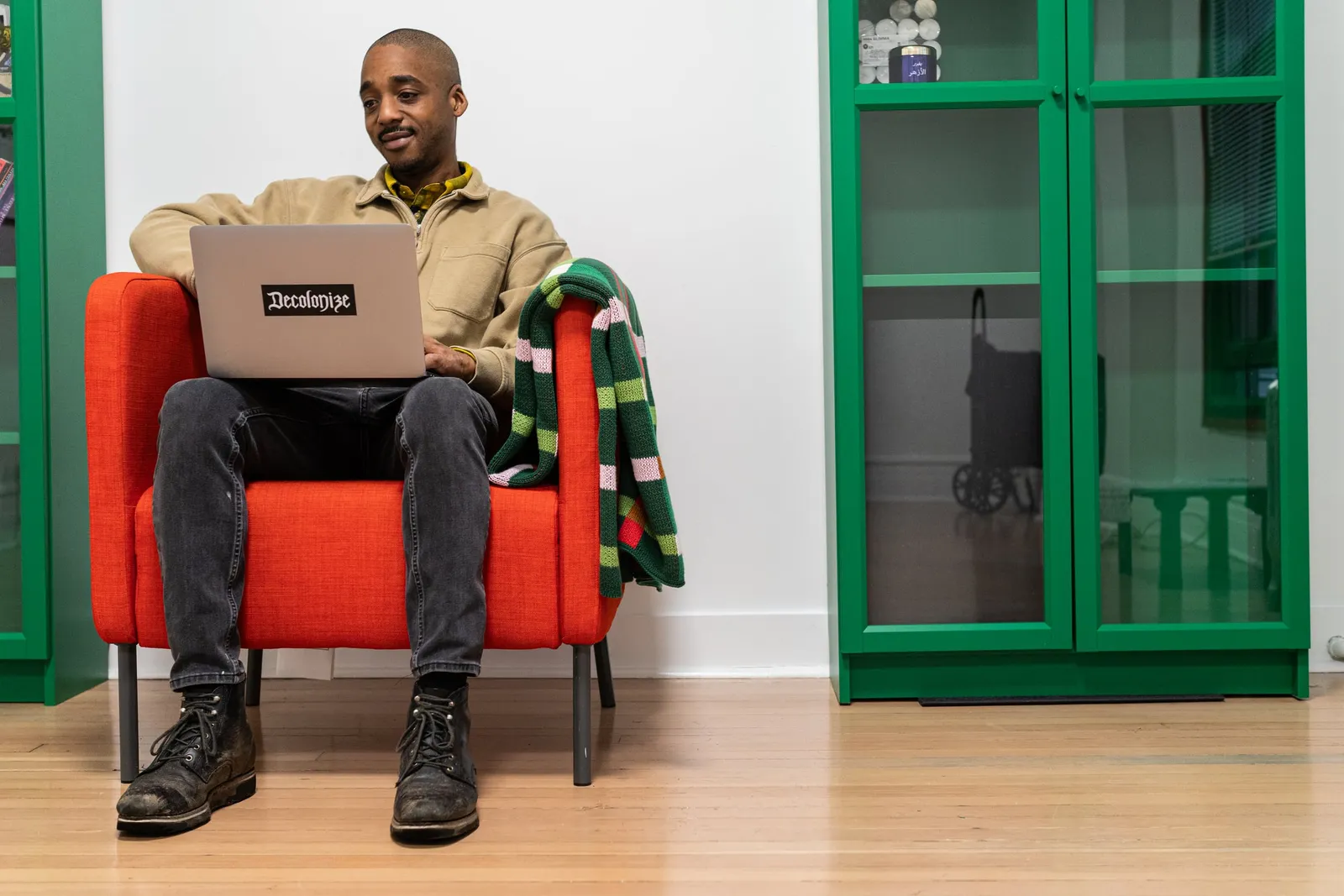 Max Harris, founder of Rize, in a red armchair with his laptop on his lap, a Decolonize sticker on the lid