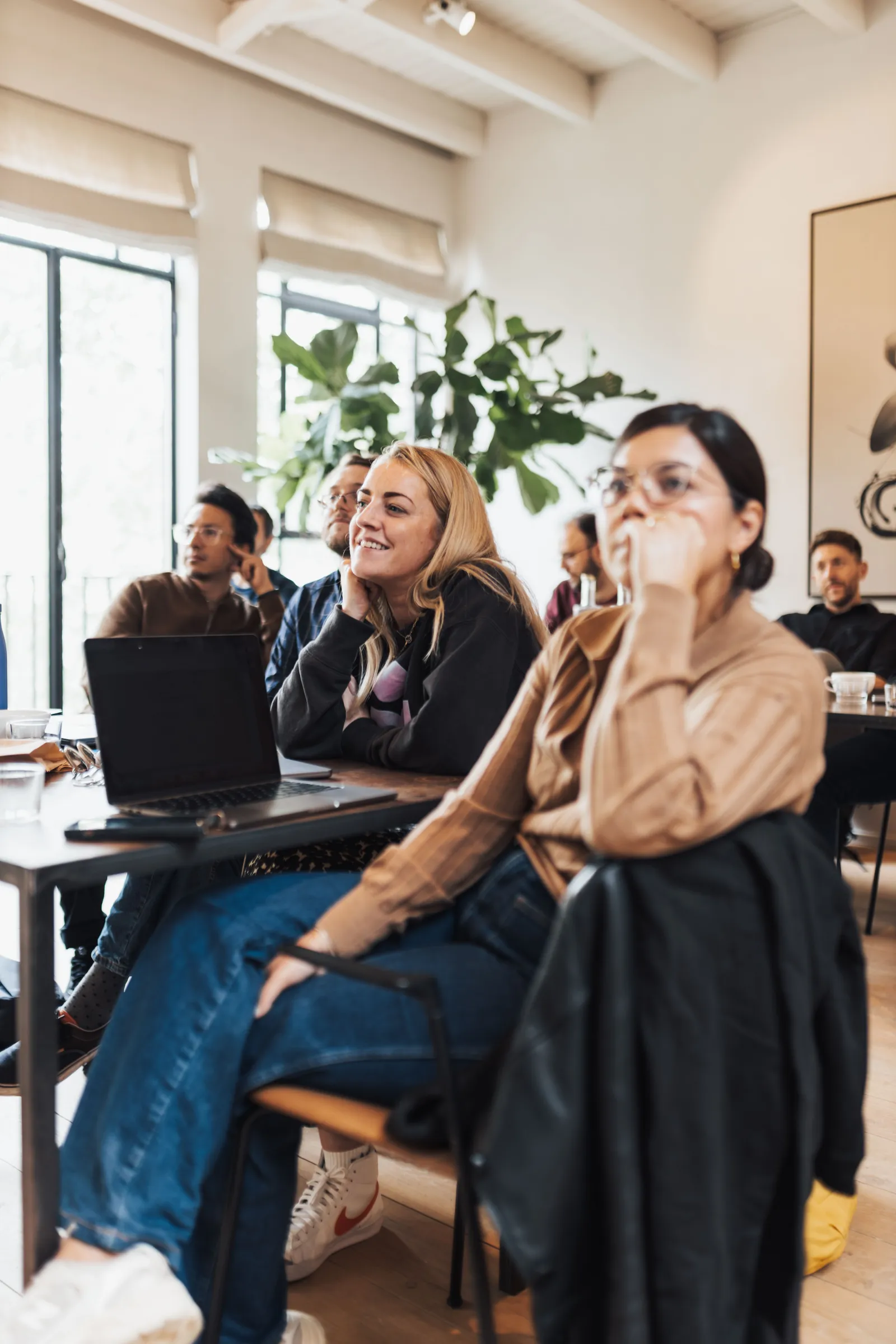 People seated around tables in a bright room, listening during a workshop