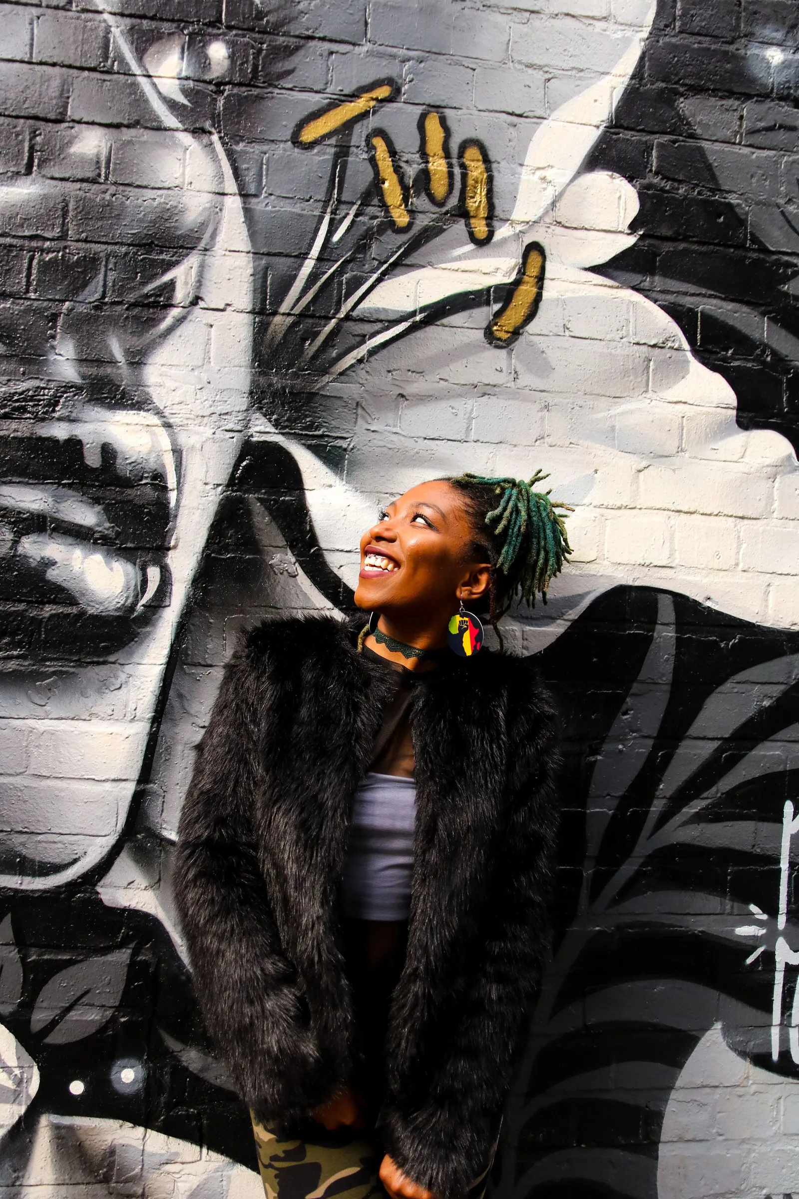 A young woman laughing and looking up in front of a black and white street mural