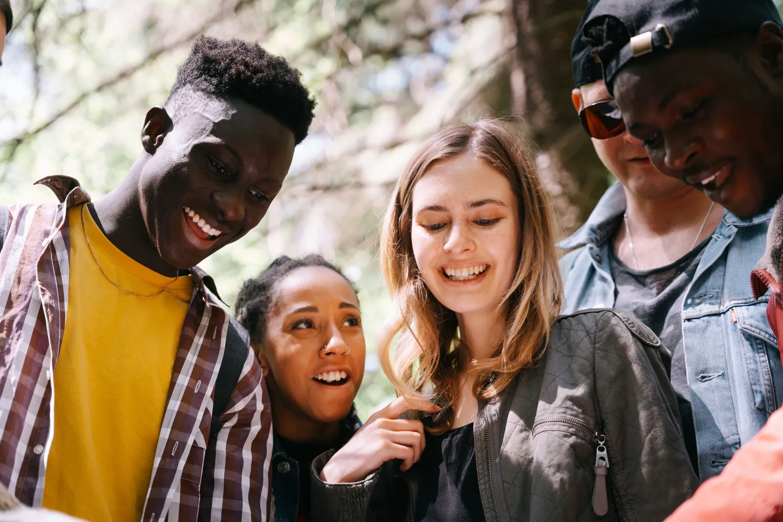 A group of young friends outdoors, laughing as they crowd in to see something