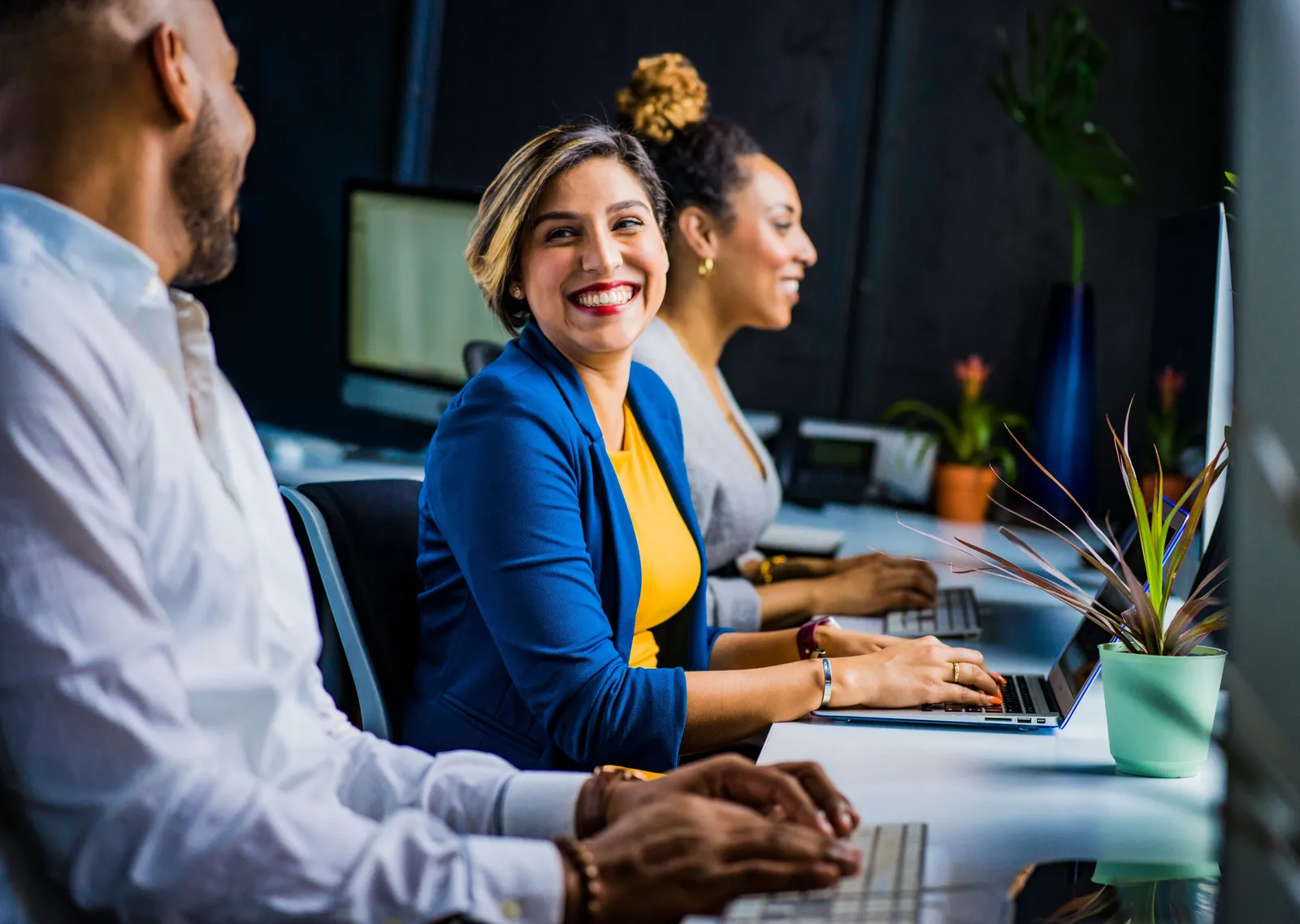 Three colleagues along a row of desks, one turning to laugh with the person beside her