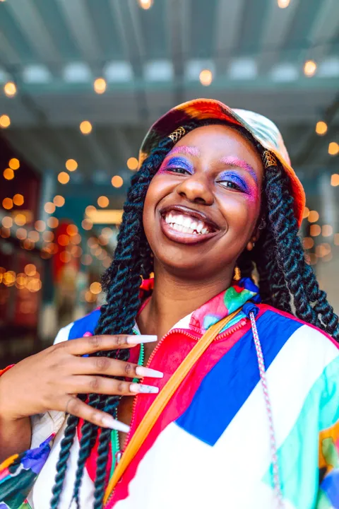 An artist in a bucket hat and colourful jacket laughing under string lights