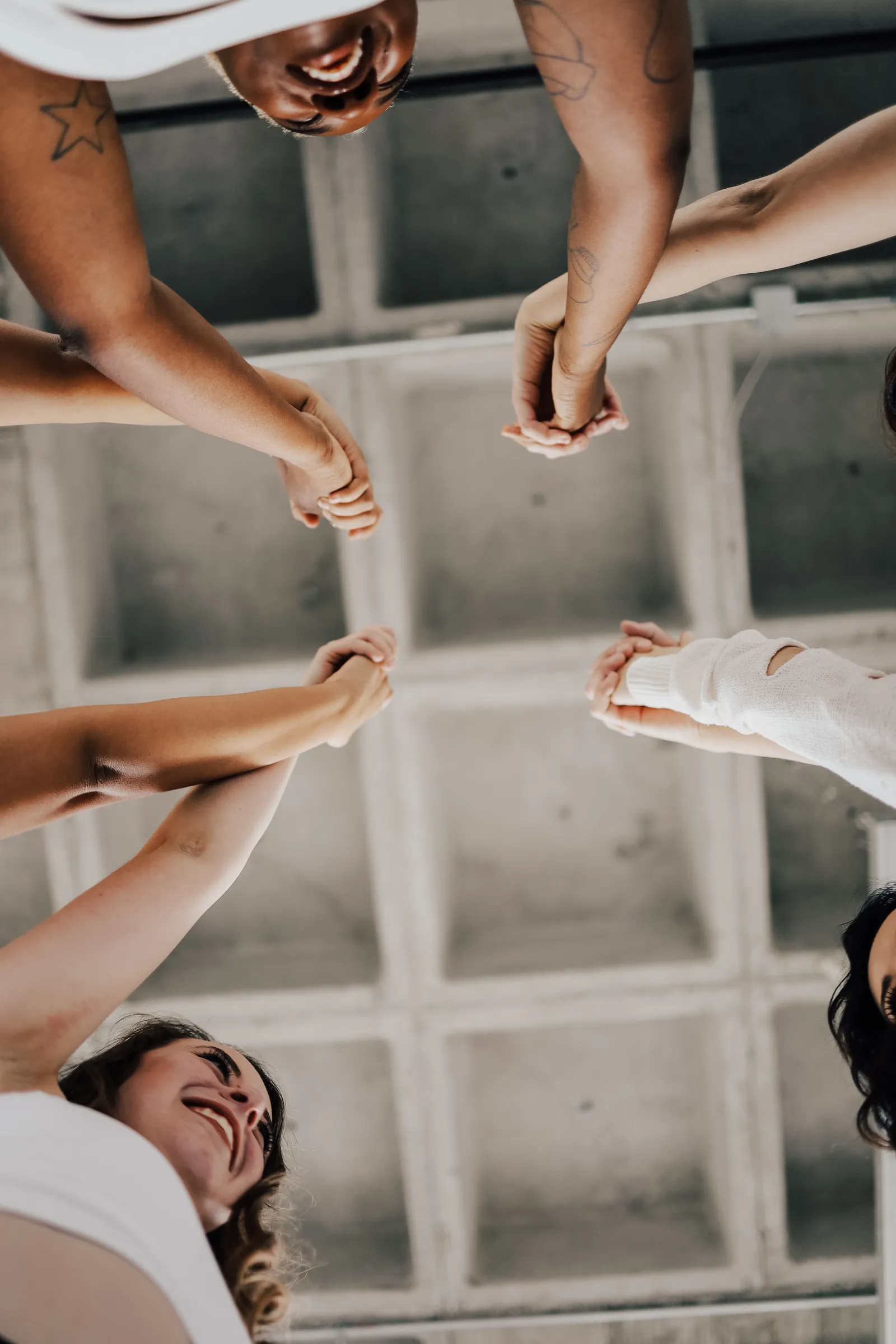 Looking up from the middle of a circle of people joining hands and laughing, under a concrete ceiling