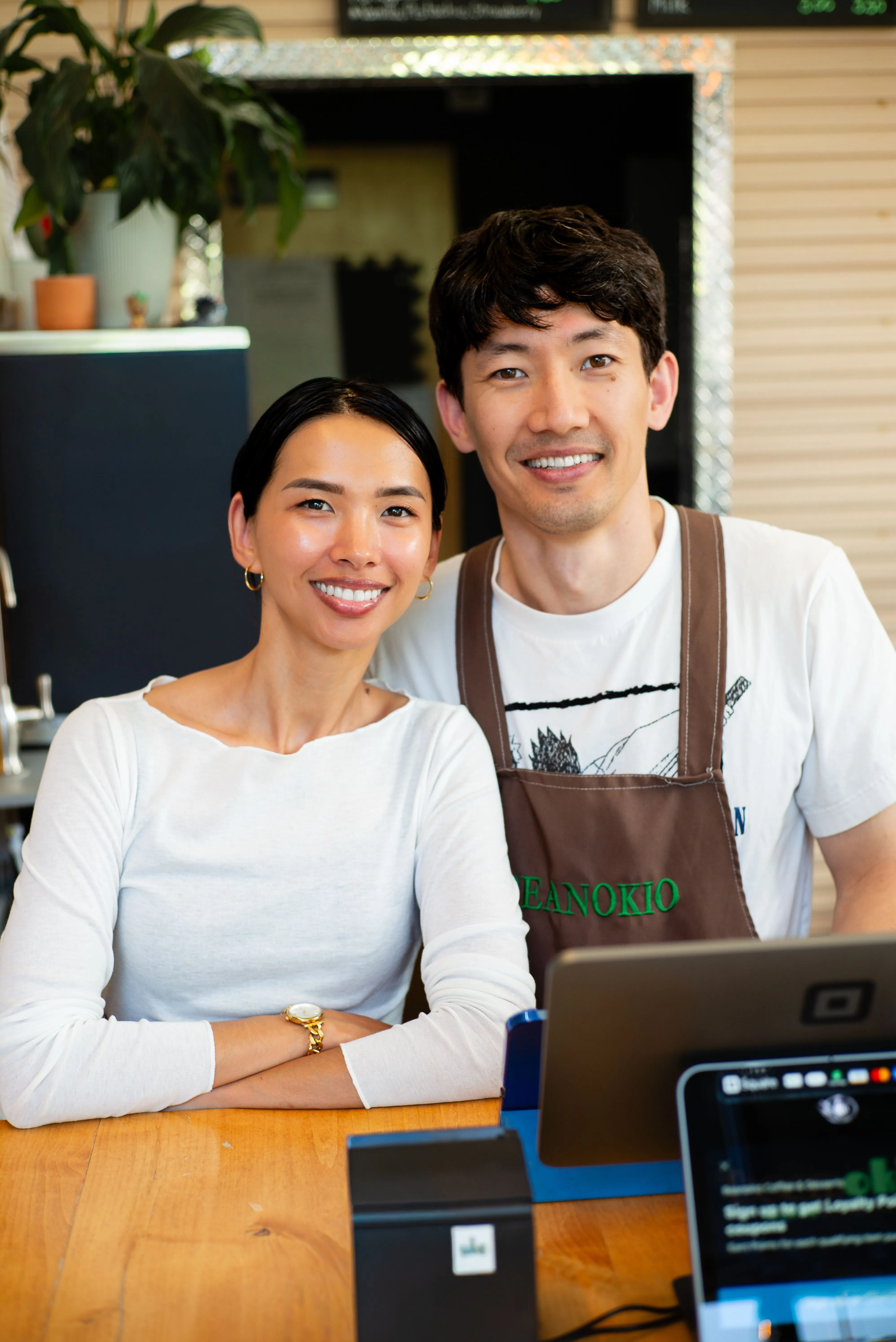 Two smiling small business owners in aprons standing in their shop