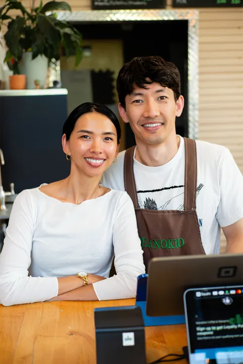 Two shop owners smiling side by side at their counter