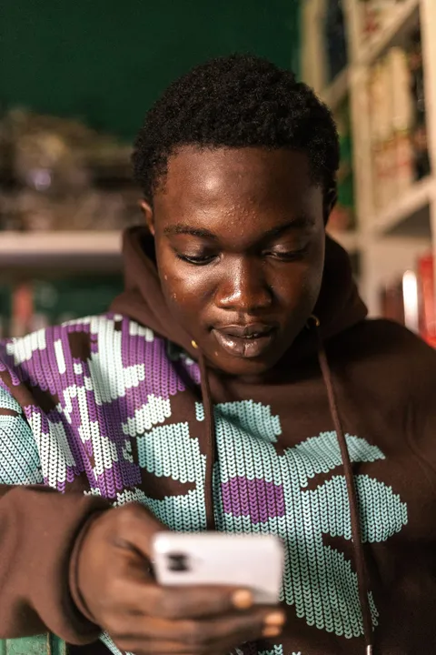 A young man in a patterned hoodie reading his phone in a shop
