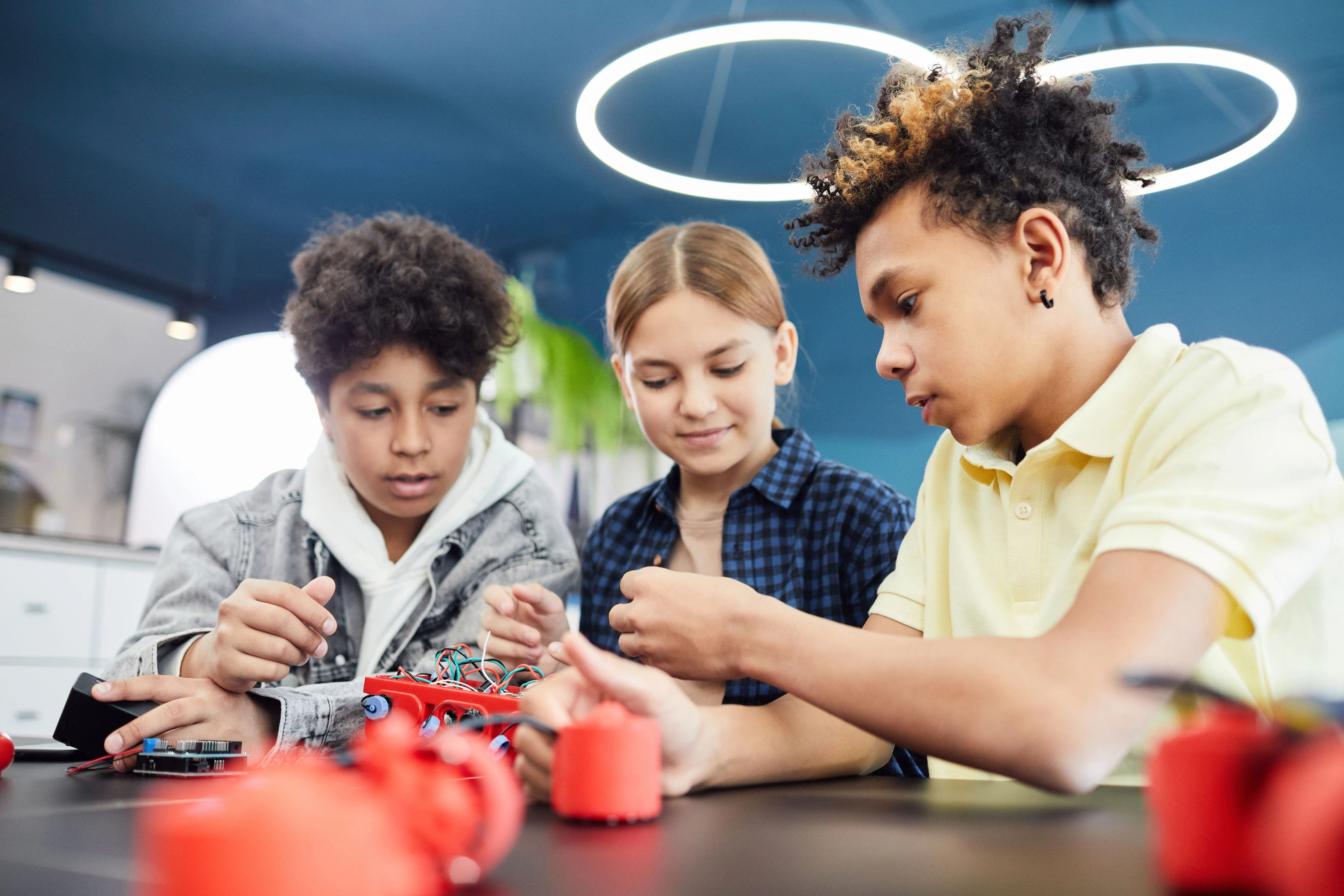 Three teenagers building a robotics project together at a workbench